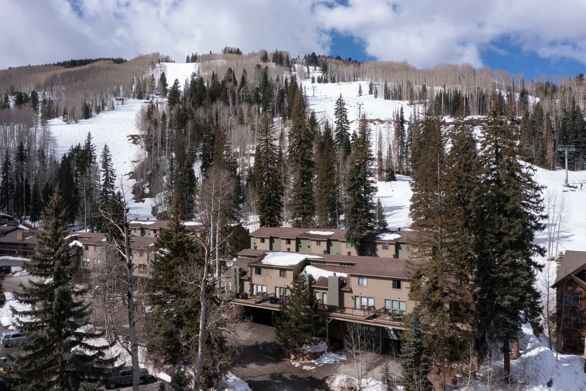 A serene winter exterior featuring snow-covered slopes, wooden resort buildings, dense pine trees, and a ski lift ascending the mountain. The landscape evokes tranquility while emphasizing the direct connection to nature and outdoor adventure.