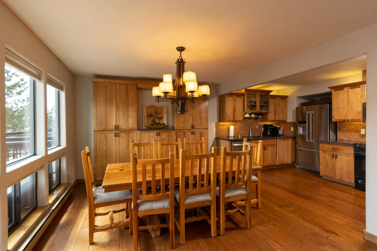 A warm, inviting dining area featuring a large wooden table surrounded by chairs, a beautiful chandelier overhead, and cabinetry in the background that hints at the adjacent kitchen. The space is styled for family meals or festive gatherings, with soft lighting enhancing the communal atmosphere.