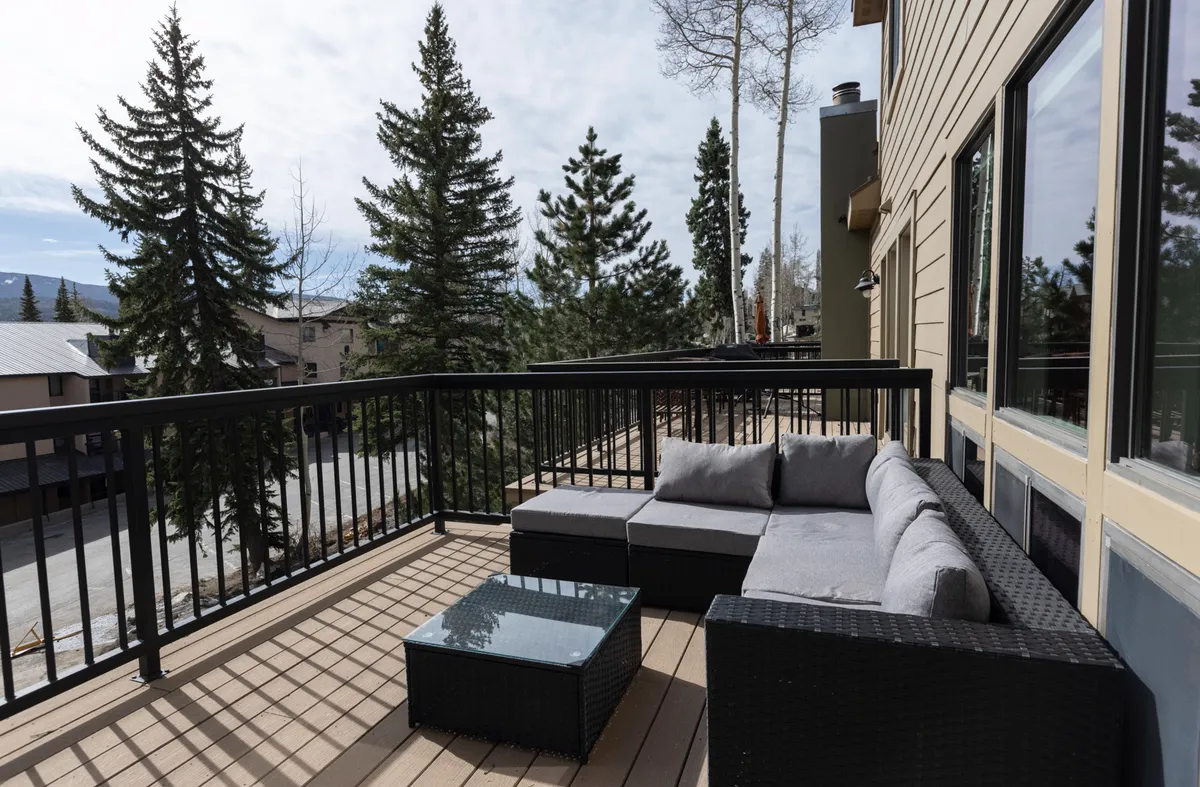 An outdoor seating area is nestled among trees, offering unobstructed mountain views. The arrangement includes a comfortable outdoor couch and a table, perfect for relaxing with sunrise coffee or stargazing under clear skies. The calm, serene ambiance emphasizes tranquility and connection with nature.