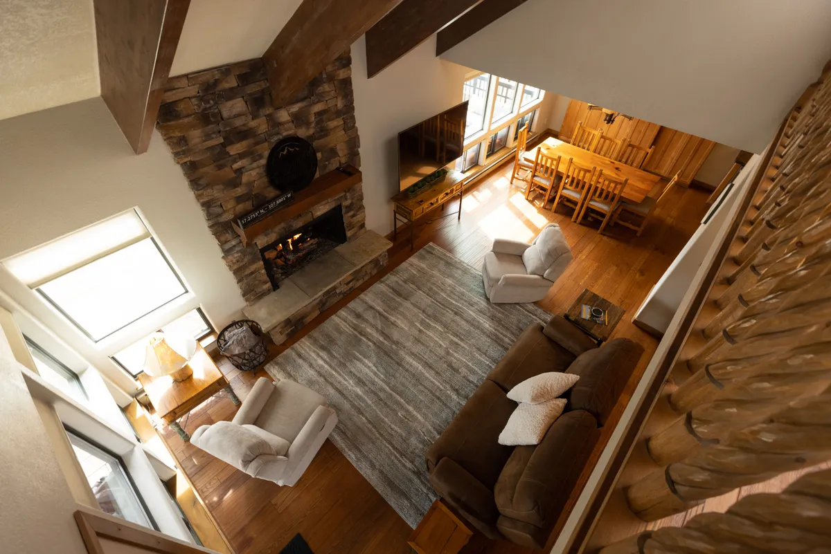 A warm and welcoming living and dining area with a central fireplace, a comfortable sofa, and expansive windows letting in natural light. The dining space is adjacent, creating an open-concept environment ideal for family gatherings and relaxation after a day on the slopes.