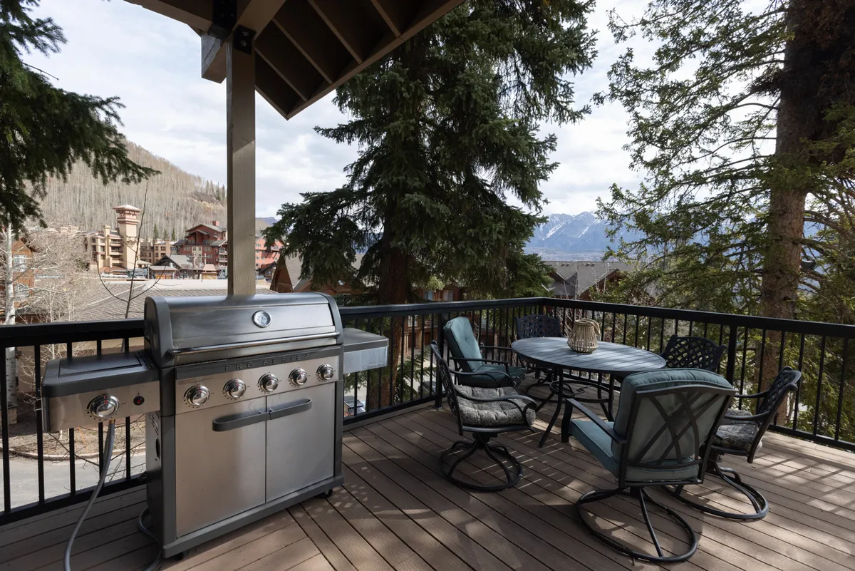 A large, inviting deck with multiple dining tables, an outdoor grill, and comfortable seating overlooks sweeping mountain vistas. The space is set up for outdoor meals, relaxation, and socializing against a breathtaking natural backdrop.